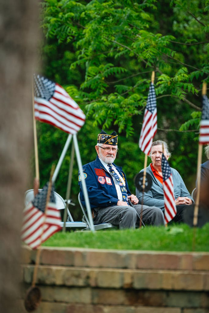 Elderly veterans sitting among American flags at an outdoor ceremony.