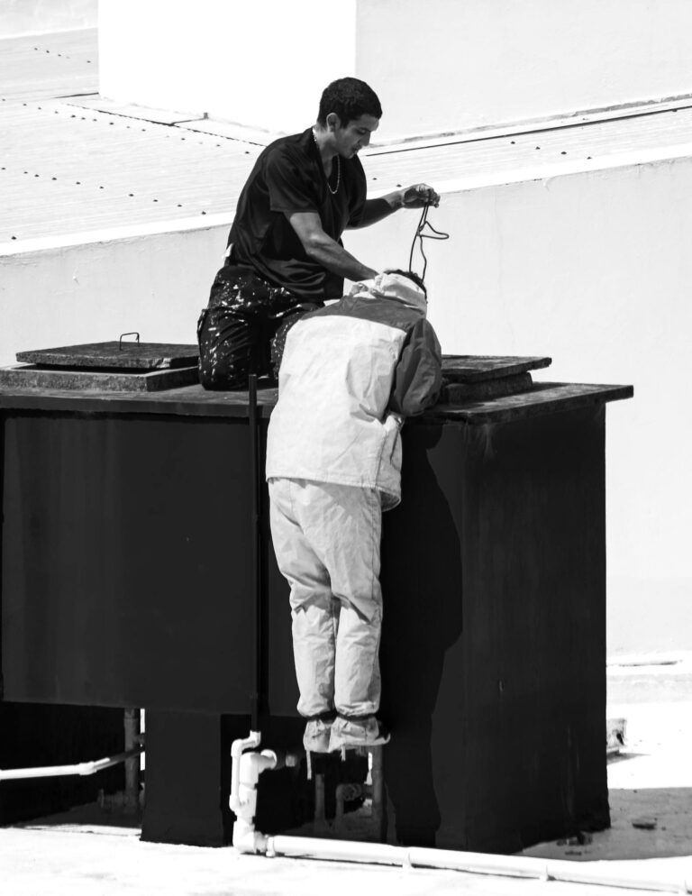 Two workers repairing rooftop water tanks in monochrome tones.